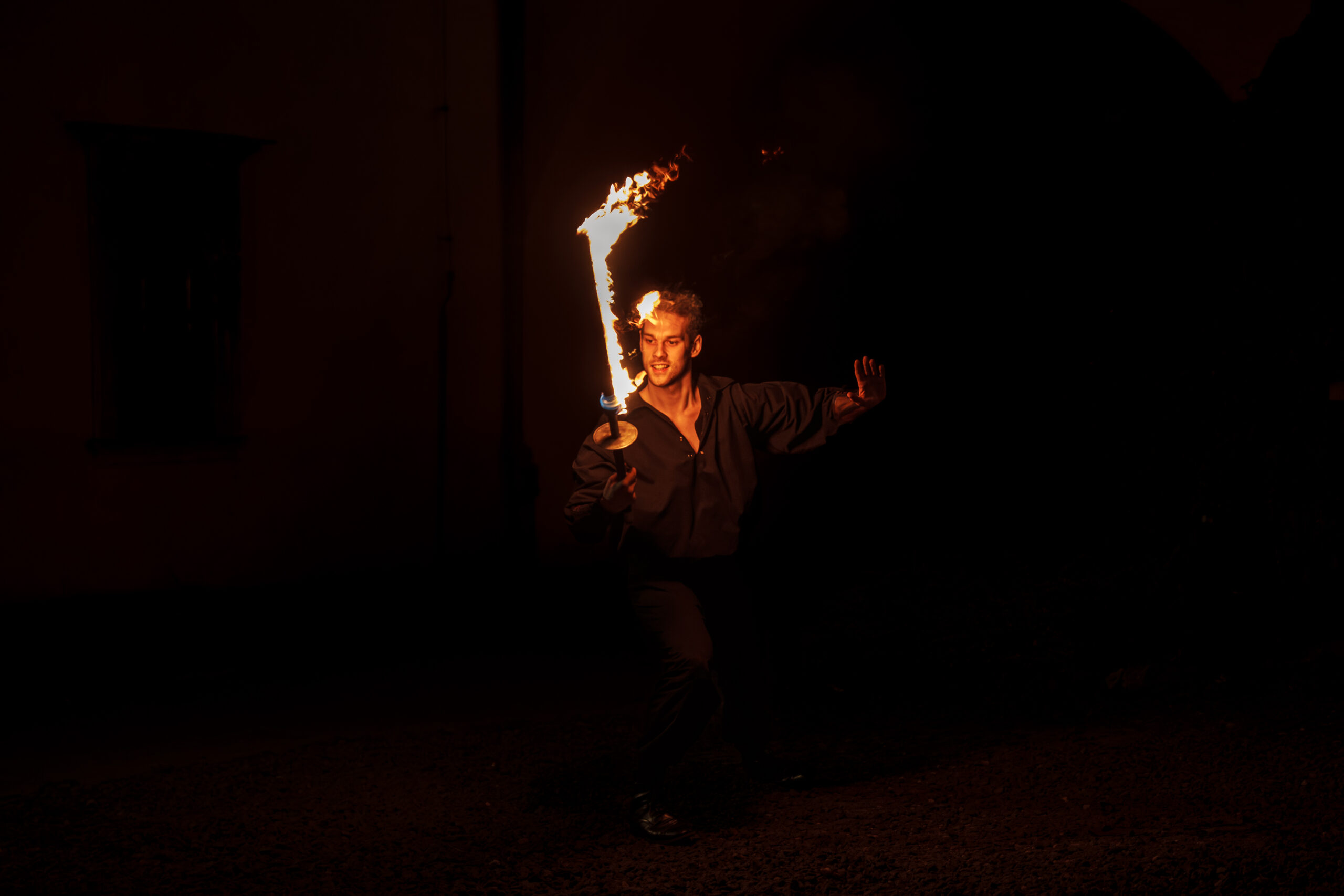 Man performing with a flaming torch at night, flames spiraling around a staff he holds