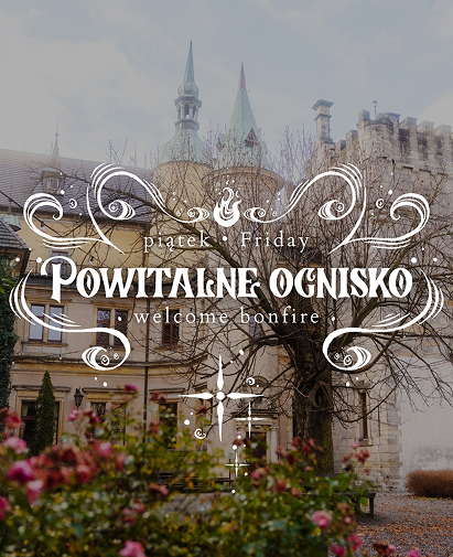 Ornate white sign reading 'Powitanie Ognisko' and 'Welcome bonfire' over a historic stone building with bare trees.