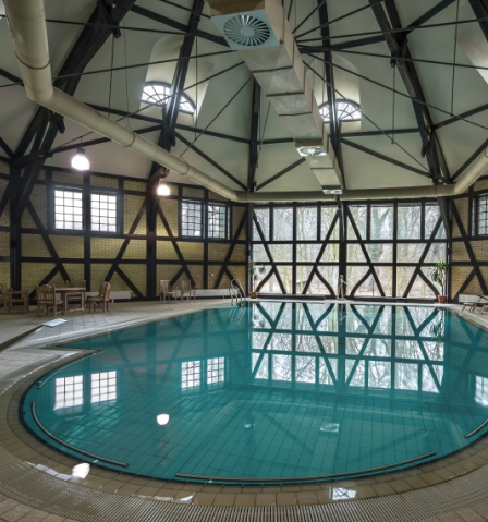 Indoor round swimming pool with turquoise water, tiled deck, and vaulted ceiling with exposed beams.