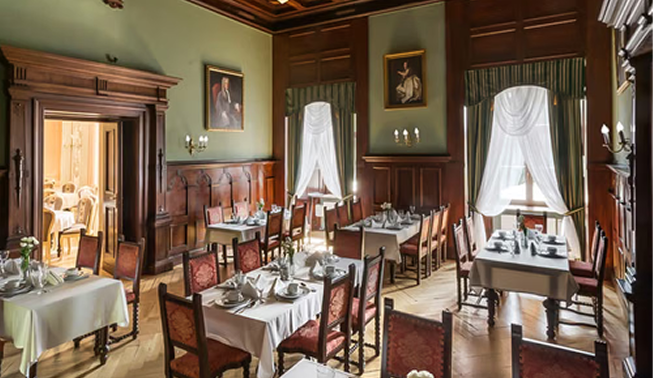 Formal dining room with white-clothed tables, wooden paneling, and red-upholstered chairs; chandeliers, paintings, and large windows with white curtains create an elegant scene.