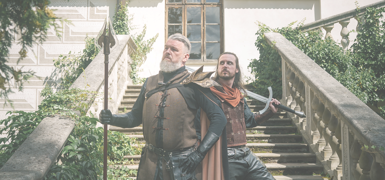Two armored men posing on a stone outdoor staircase, one holding a spear and the other a curved sword, with ivy around them.