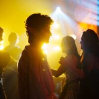 Silhouetted person in a sparkly costume wearing elf ears at a neon-lit party with yellow and blue lights.
