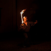 Man performing with a flaming torch at night, flames spiraling around a staff he holds