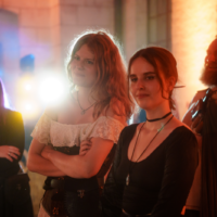 Group of five friends at a party or concert, smiling and facing the stage with warm orange lights behind them.