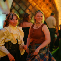 Two women in vintage costumes dancing at a costume party with warm, colorful lighting.
