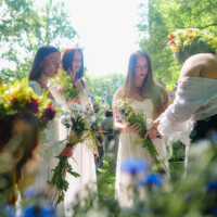 Four women in white dresses standing in a sunlit garden, each holding a bouquet of wildflowers.