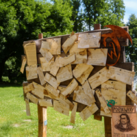 Wooden display covered with handwritten notes and letters in a sunny park, with a Polish 'POSZUKIWANY' poster on the lower right.