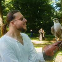 Man with a glove holds a falcon on his arm, smiling in a sunny park.