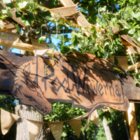 Hand-carved wooden sign with a wolf head, hanging on a wooden frame adorned with ivy and burlap bunting in a sunny outdoor setting.