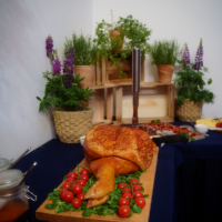 Roast meat centerpiece on a wooden board garnished with greens and cherry tomatoes, knife standing upright in the meat.