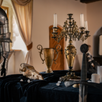 Medieval still life on a velvet table: knight armor, skull, dagger, and a gilded candle chandelier.
