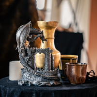 Dragon ruin sculpture as a table centerpiece with a brass vase and copper cups on a dark cloth table