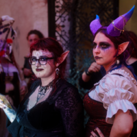 Two women in fantasy costumes with elf ears and dramatic makeup at a dimly lit party venue.