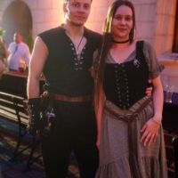 Couple in medieval/fantasy costumes posing together outdoors at dusk.